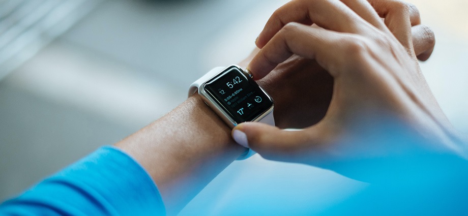 A woman wearing a smartwatch and holding a smartphone displaying a health app, representing the use of digital health tools for managing personal health.